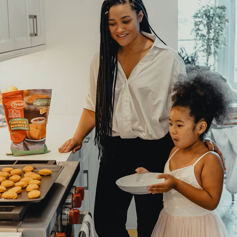 Lisa and her daughter Emma preparing chicken nuggets together in their kitchen with smiles and teamwork.